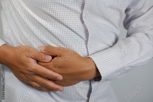 Close-up. A man's hand is holding his stomach and massaging it. The man in the shirt and shirt is experiencing abdominal pain on the right side. The sick man is suffering from liver disease, gastritis