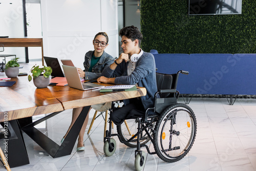 Latin young man in wheelchair working at office in Mexico Latin America, hispanic coworkers and business teamwork in concept of disability and disabled person