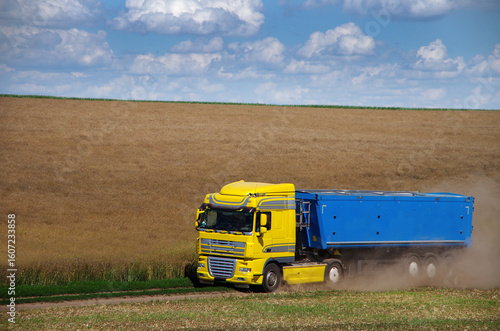 Truck - container in a rapeseed field in motion raises clouds of dust, harves...