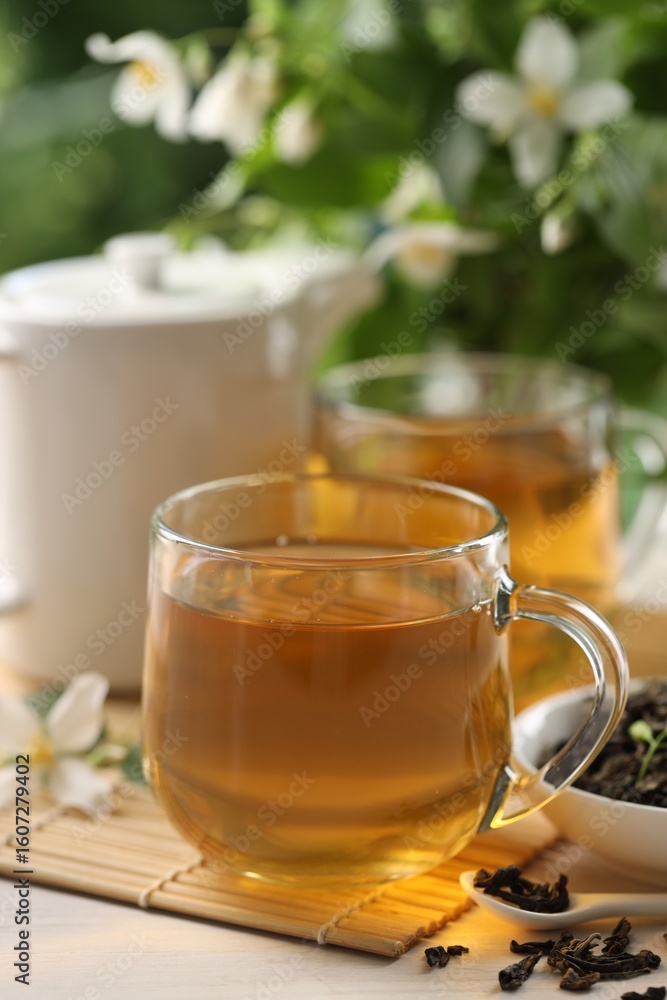 Tasty jasmine tea in cups, teapot, dry leaves and flowers at white wooden table, closeup Tasty jasmine tea in cups, teapot, dry leaves and flowers at white wooden table, closeup