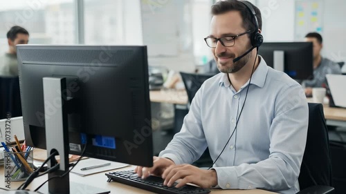 Professional male customer service representative in headset working on computer in bright modern office