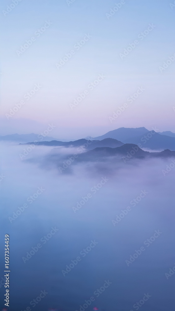 Fototapeta premium Tranquil mountain landscape covered in soft morning mist, blue and purple tones, peaceful dreamy nature scenery for vertical mobile wallpaper or digital mindfulness background