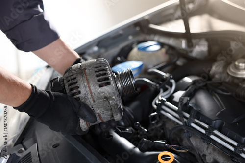 Auto part. Professional mechanic with alternator near open hood of car indoors, closeup