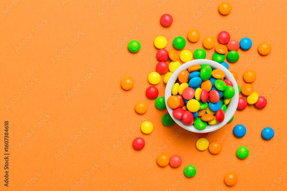 Obraz premium Multicolored candies in a bowl on a colored background. birthday and holiday concept. Top view with copy space
