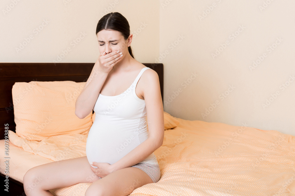 Pregnant suffering with nausea. Pregnancy symptoms, expectation toxicosis. Young vomiting woman sitting on bed. parenthood concept Pregnant suffering with nausea. Pregnancy symptoms, expectation toxicosis. Young vomiting woman sitting on bed. parenthood concept