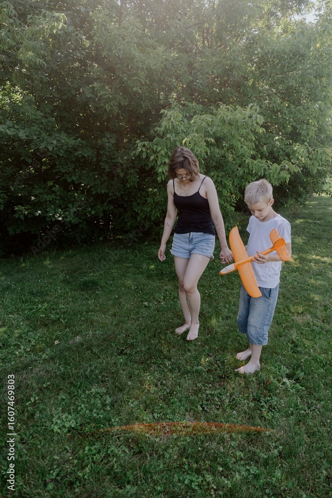 Fototapeta premium A mother and her son with hearing aids launch a paper airplane in a park, a heartwarming moment of inclusive play and bonding in nature. Perfect for disability awareness and family lifestyle content