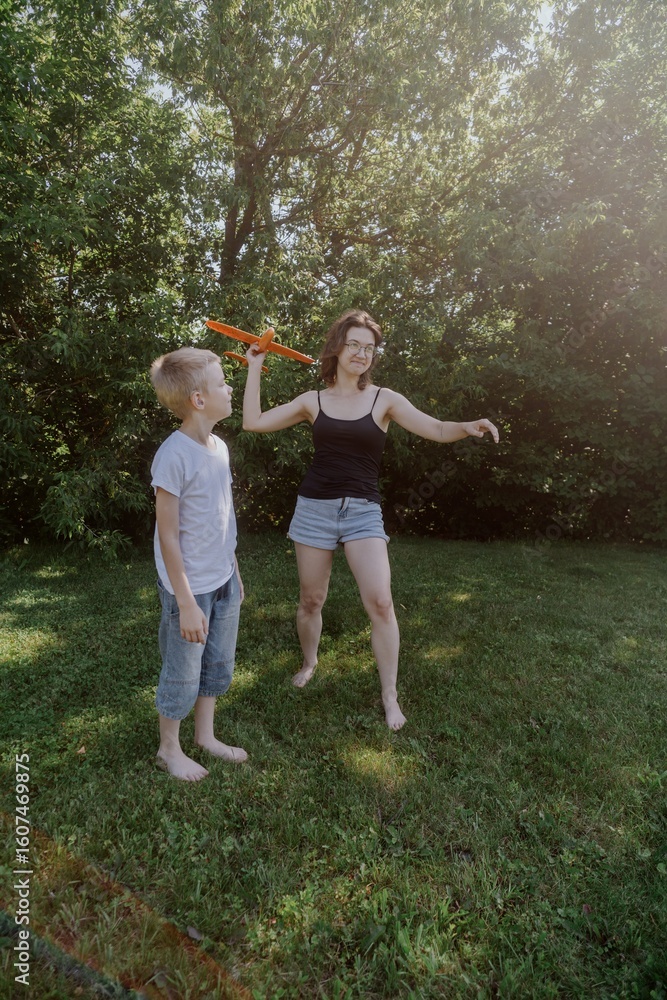 Fototapeta premium A mother and her son with hearing aids launch a paper airplane in a park, a heartwarming moment of inclusive play and bonding in nature. Perfect for disability awareness and family lifestyle content