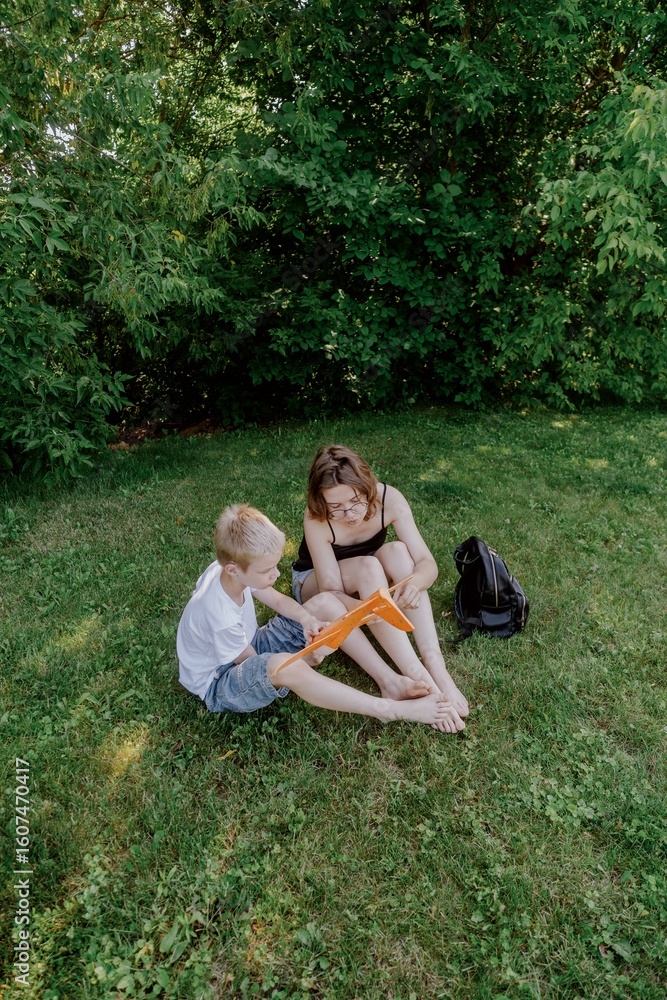 Fototapeta premium A mother and her son with hearing aids launch a paper airplane in a park, a heartwarming moment of inclusive play and bonding in nature. Perfect for disability awareness and family lifestyle content