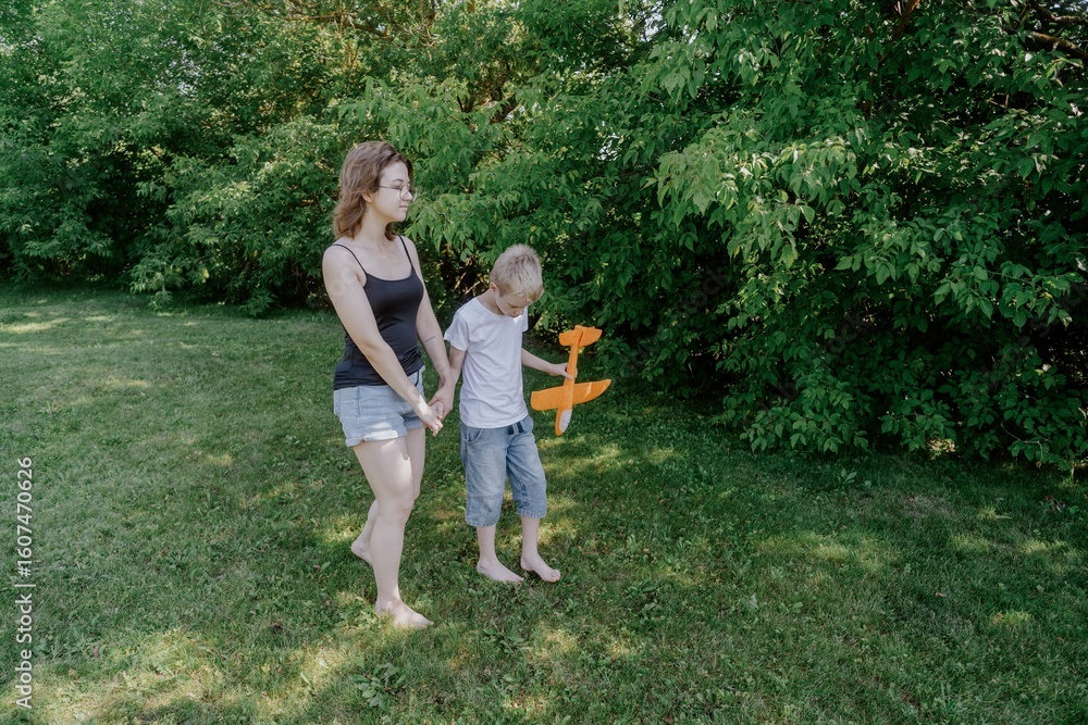 Fototapeta premium A mother and her son with hearing aids launch a paper airplane in a park, a heartwarming moment of inclusive play and bonding in nature. Perfect for disability awareness and family lifestyle content
