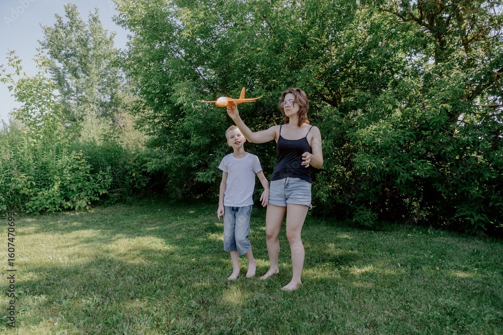 Obraz premium A mother and her son with hearing aids launch a paper airplane in a park, a heartwarming moment of inclusive play and bonding in nature. Perfect for disability awareness and family lifestyle content