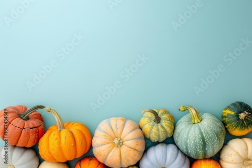 A variety of pumpkins arranged at the bottom of a pale blue surface. Top half of the image is solid blue with free space.