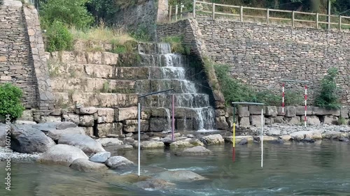 Small waterfall cascading over stone wall into river


