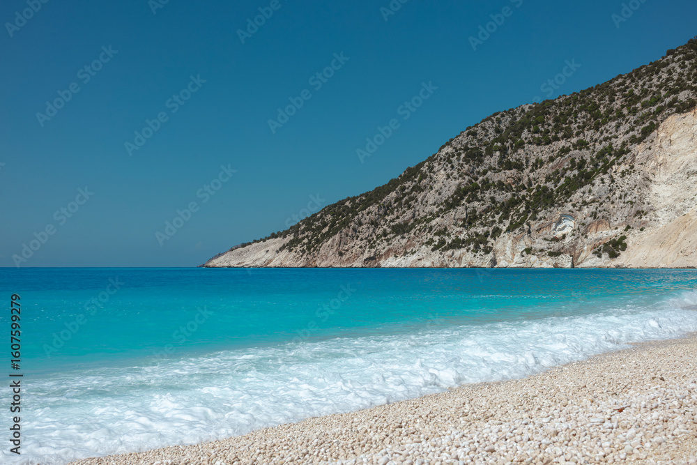 Naklejka premium Turquoise Mediterranean waves gently washing onto white pebble beach with limestone cliffs
