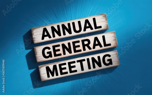 Annual General Meeting Concept Showing Text On Wooden Blocks Against a Blue Textured Background With Sunburst Lighting