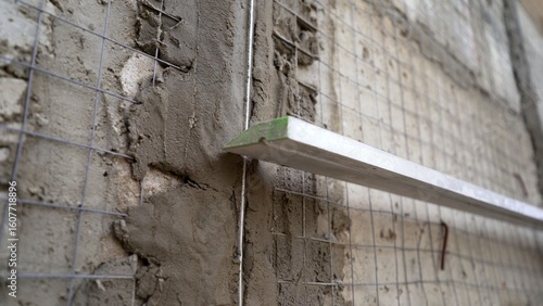 Construction worker plastering a wall using metal lath and a long leveling tool for a smooth finish