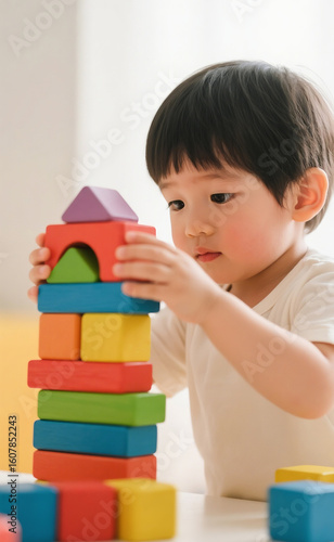 Focused young Asian boy building a tower with colorful wooden blocks. Early childhood development and learning through play concept.