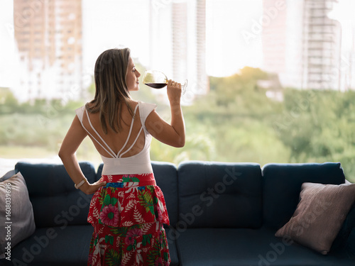 Mujer disfrutando una copa de vino junto a la ventana en un apartamento moderno