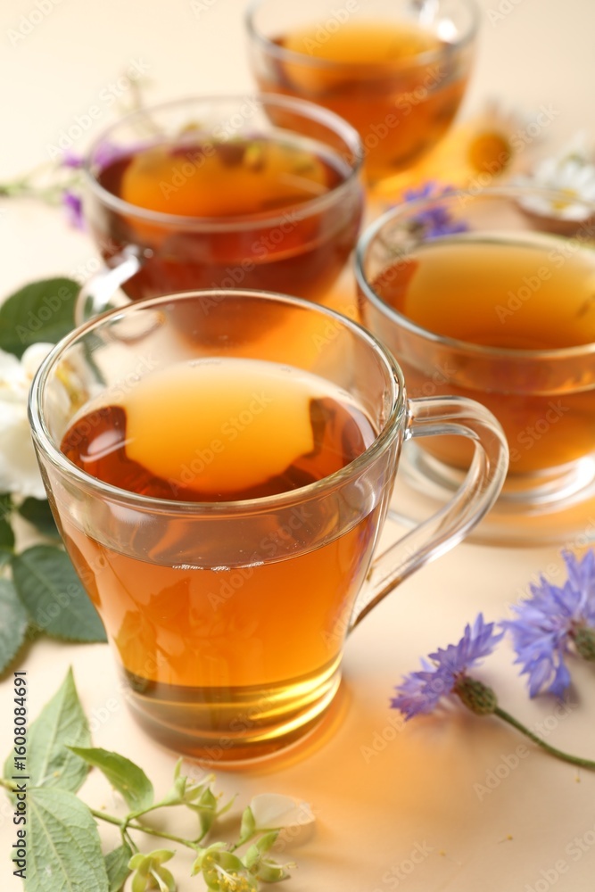 Aromatic herbal tea in glass cups and different flowers on beige background, closeup Aromatic herbal tea in glass cups and different flowers on beige background, closeup
