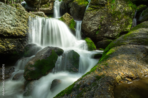 Cascading waterfall flows over moss-covered rocks, creating a serene natural scene with vibrant greenery and smooth water textures, perfect for relaxation and tranquility