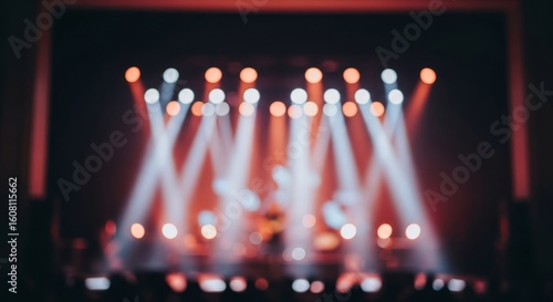 Blurred view of a stage with bright spotlights shining down on a performance, with an audience in the foreground.