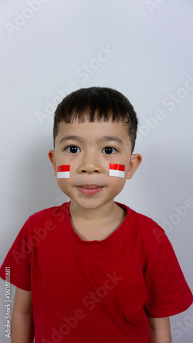 Close-up portrait of an Asian boy wearing a red top and a sticker on his face, isolated on a white background. Indonesian Independence Day concept.