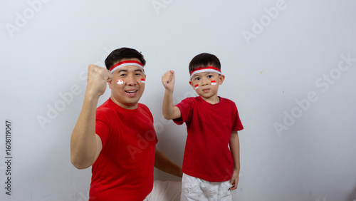 Asian father and son with happy and cheerful expressions wearing red tops and headbands while raising their right fists in front of them as a symbol of spirit, isolated on a white background. Indonesi