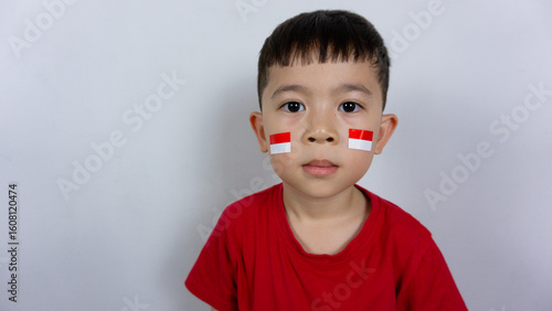 Close-up portrait of an Asian boy wearing a red top and a sticker on his face, isolated on a white background. Indonesian Independence Day concept.