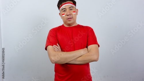 Portrait of a confident young Asian man wearing a red t-shirt and Indonesian flag headband standing with crossed arms. Indonesian Independence Day concept.