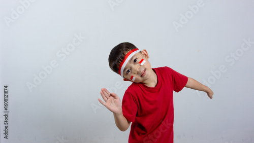 A cheerful Indonesian boy wearing a red top and headband, a mini Indonesian flag sticker on his face, posing hello and smiling, isolated on a white background. Indonesian Independence Day concept.
