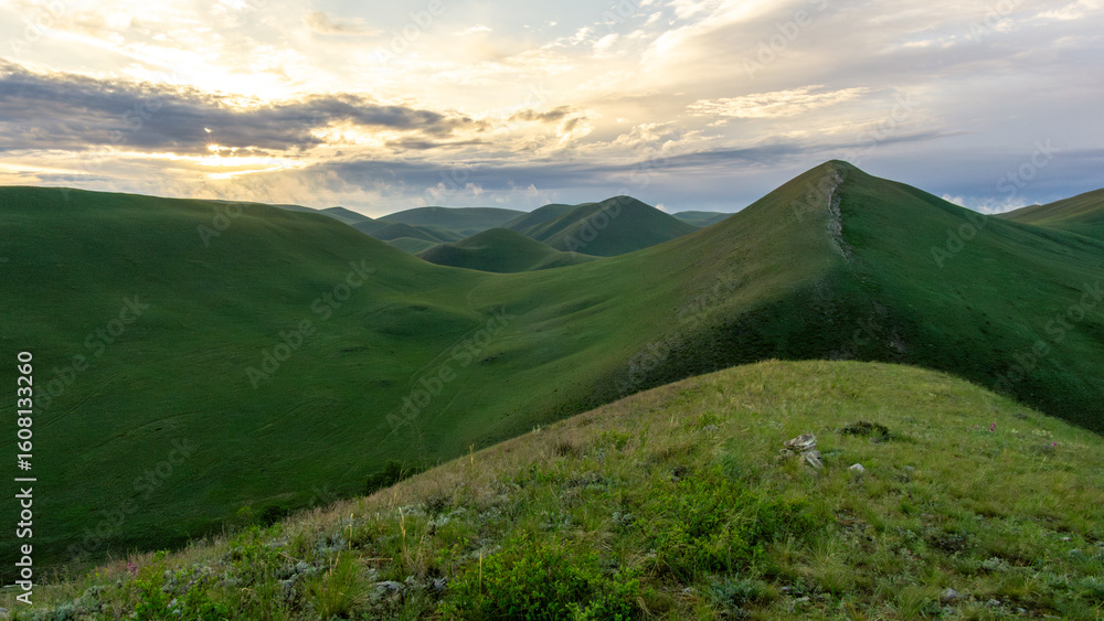 Expansive green hills under a dramatic sky at sunset, showcasing rolling landscapes and vibrant vegetation, creating a serene and tranquil natural environment Expansive green hills under a dramatic sky at sunset, showcasing rolling landscapes and vibrant vegetation, creating a serene and tranquil natural environment