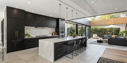 Open-concept modern kitchen with black cabinets, waterfall island, and connected living room in the background
