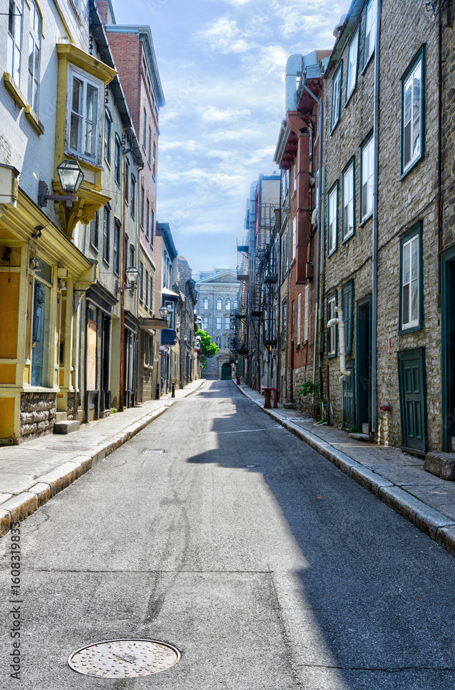 Fototapeta premium Charming street in Old Quebec with historic buildings, colorful facades, and a bright summer sky. Perfect for travel, editorial, or architectural design concepts. Peaceful and timeless atmosphere.
