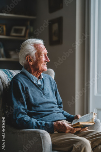 elderly man sits in cozy armchair holding book lost in tender memories of his youth