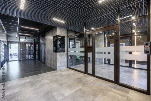 Modern lobby featuring tile floors, glass doors, a grid ceiling with lights, and a security system