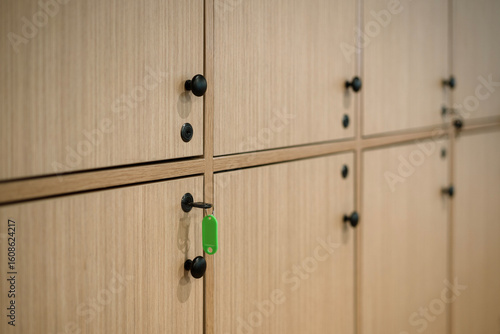 Close-up of light wood lockers with black knobs. A key with a green tag is in one lock, focusing on storage, security, and access in a gym or spa.
