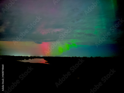 Northern lights over the missouri river with a rural town in the background. aurora borealis green red with clouds 