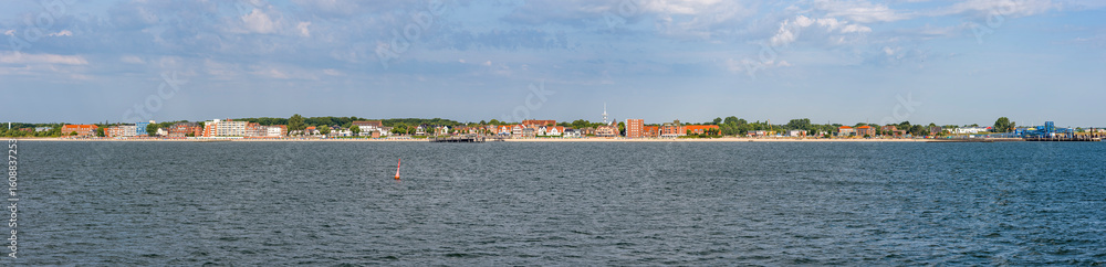 Obraz premium Panoramafoto von Wyk auf Föhr bei schönem, sonnigen Wetter mit Strandpromenade, Hafen und Gebäuden vom Meer aus gesehen mit dem Wasser der Nordsee im Vordergrund