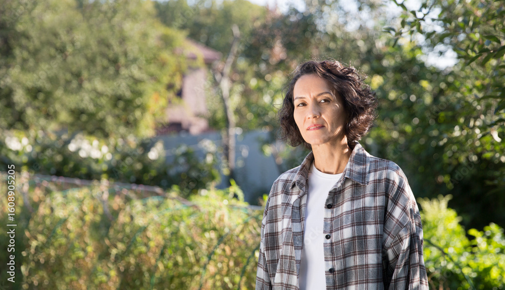 Happy middle aged woman in a plaid shirt stands in her garden on a summer day Happy middle aged woman in a plaid shirt stands in her garden on a summer day