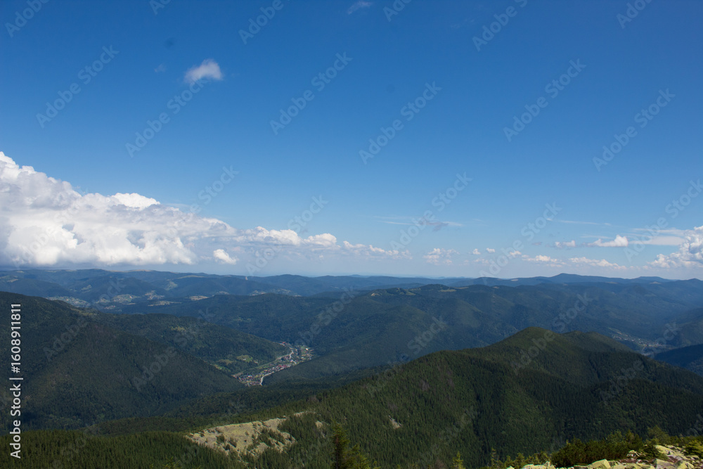 Fototapeta premium Panoramic view of endless forested mountain ridges and valleys under bright blue sky with white clouds