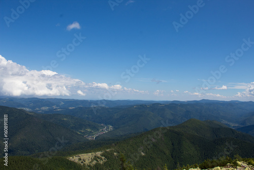 Panoramic view of endless forested mountain ridges and valleys under bright blue sky with white clouds
