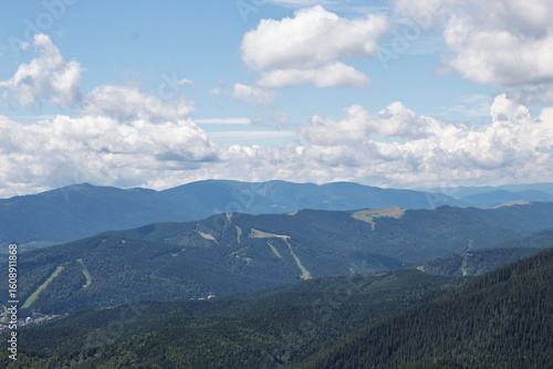 Mountain ski resort with visible slopes and lifts nestled among forested ridges under dramatic cloudy sky