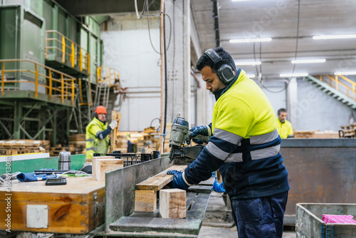 Quadro su tela Carpenter wearing safety equipment using pneumatic nail gun assembling wooden pa