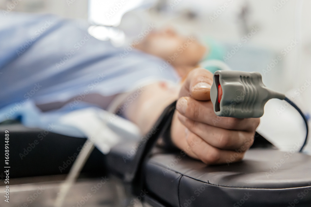Fototapeta premium Patient lying on examination table in medical facility, with hand holding pulse oximeter, showcasing healthcare technology and patient monitoring in clinical environment