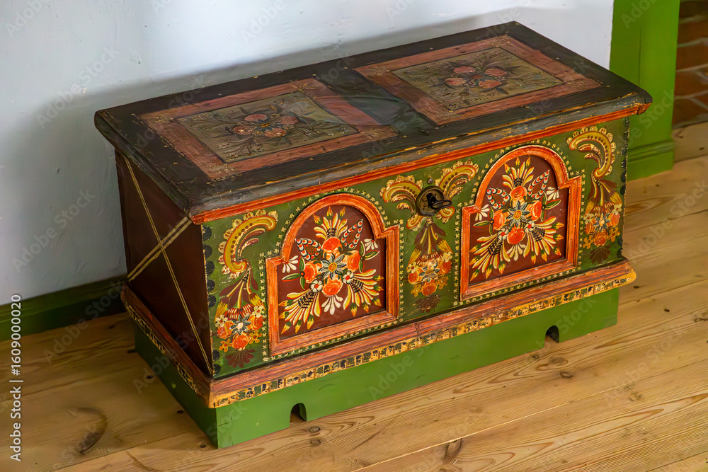 Ταπετσαρία Colorful hand-painted wooden dowry chest decorated with traditional floral folk motifs, placed on a wooden floor in a rustic village interior
