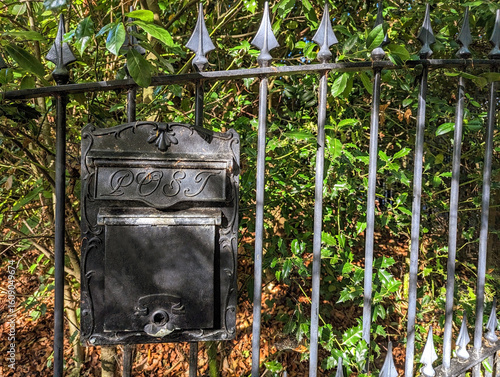 Old classical style black metal letter box hanging on a wrought iron fence on the exterior of a residential property