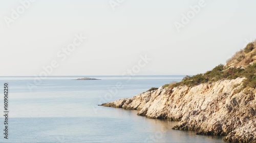 Wallpaper Mural Peaceful sea view with rocky shore in the foreground and a small rocky island on the horizon. Bright clear sky adds to the tranquil mood. Filmed in Varkiza, Athens, Greece. No people. Torontodigital.ca