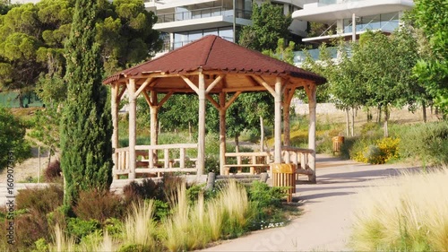 Wallpaper Mural Close-up of a wooden gazebo with brown roof in lush public park in Varkiza, Athens, Greece. Surrounded by green plants, including Nassella tenuissima and Apodasmia similis. No people visible. Torontodigital.ca