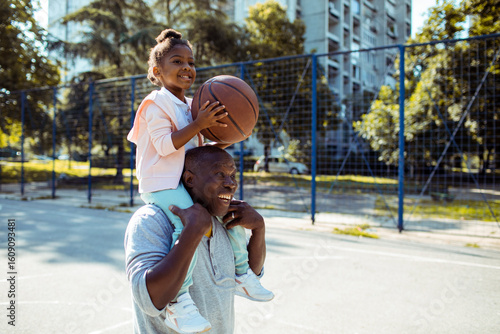Grandfather teaching granddaughter how to play basketball outdoors