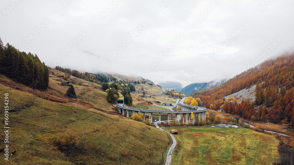 Naklejka premium Mountain landscape in the Aosta valley near the Great St Bernard Tunnel. Aerial view of misty slopes and autumn forest in the Alps.
