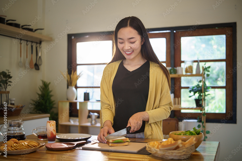 Fototapeta premium Smiling asian young woman making a healthy sandwich with vegetables and bread.